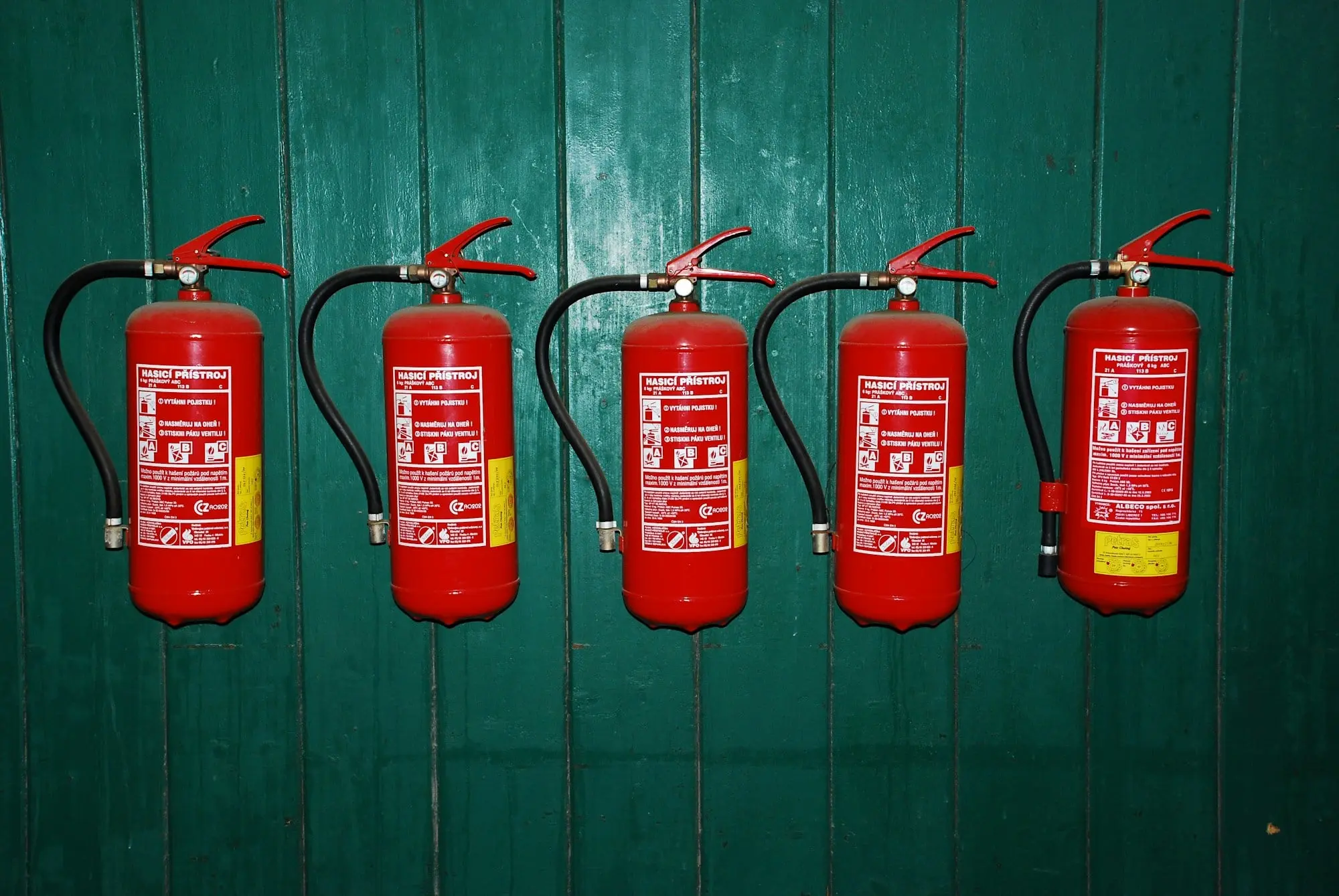 Five red fire extinguishers in a row on a green wall